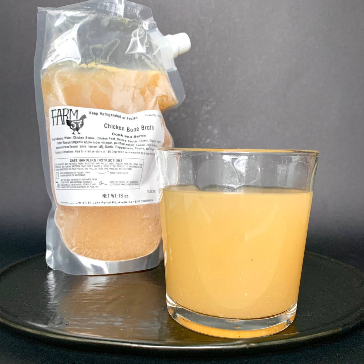 pour spout pouch of broth standing behind a glass of poured broth on a plate