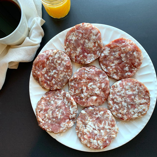 A plate of raw breakfast patties arranged on a plate, styled next to a cup of coffee and orange juice