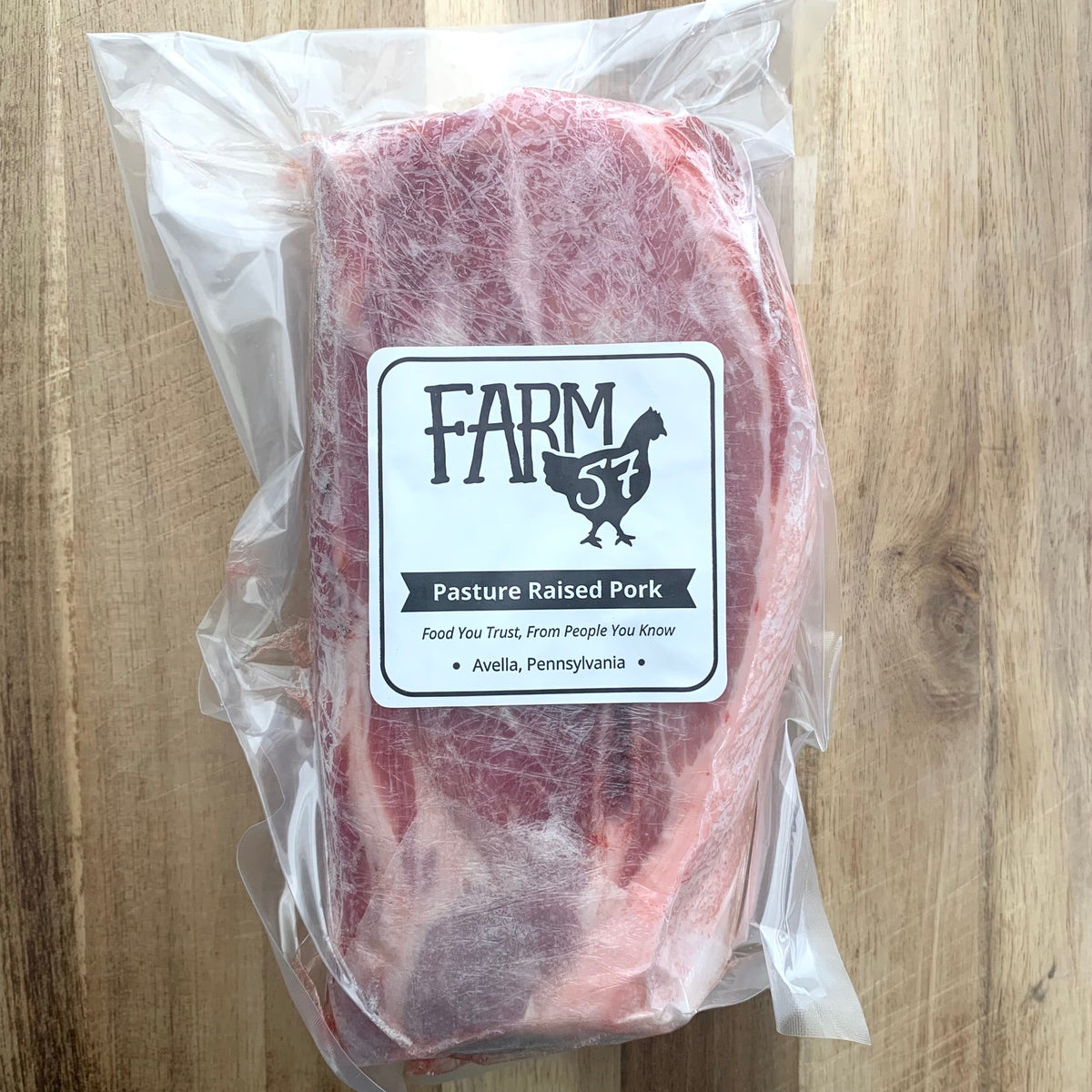 vacuum sealed and frozen package of pork shoulder roast on a wood cutting board, with farm57 label