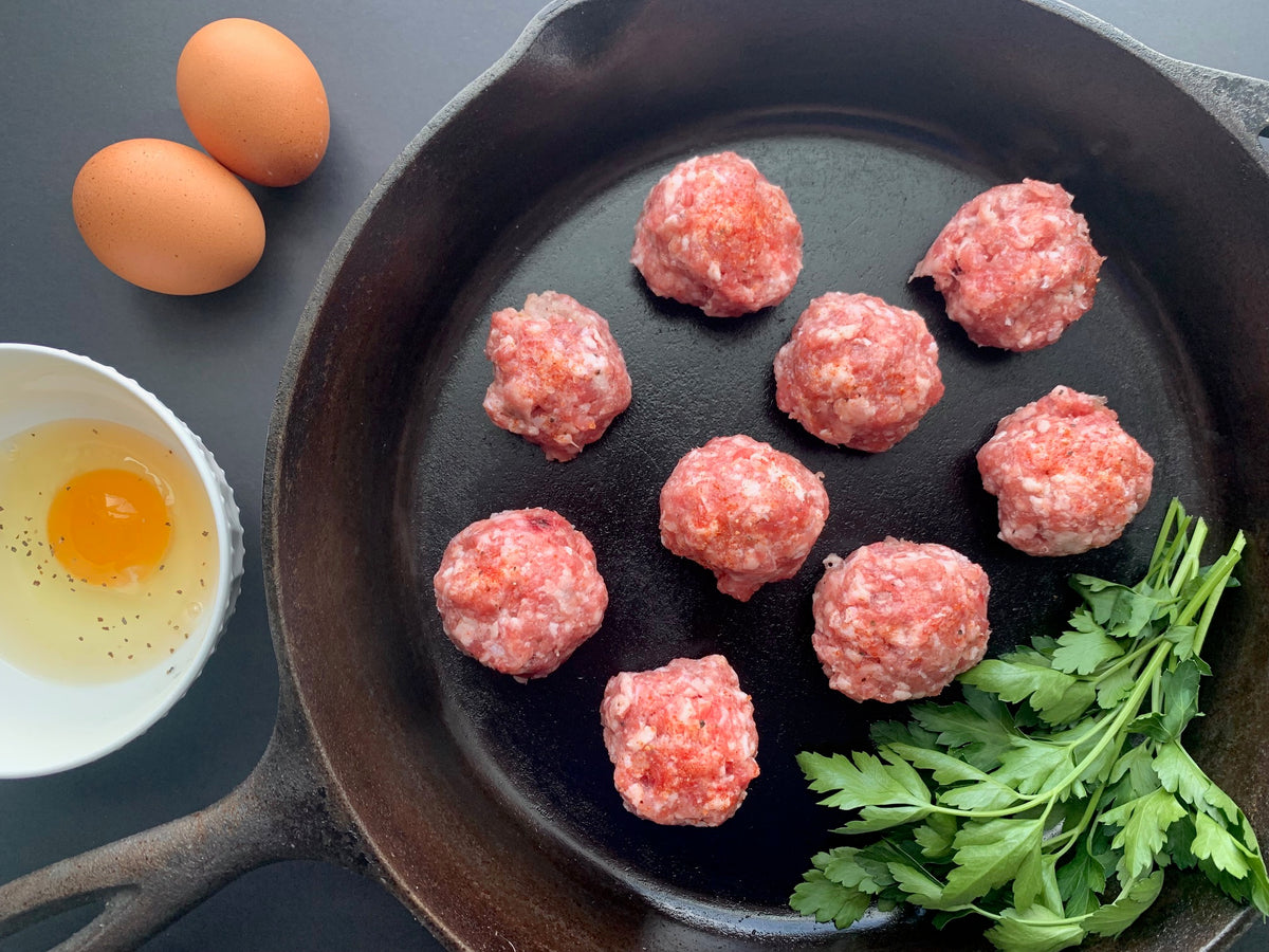 raw ground sausage in a pan styled beside a cracked egg and herbs