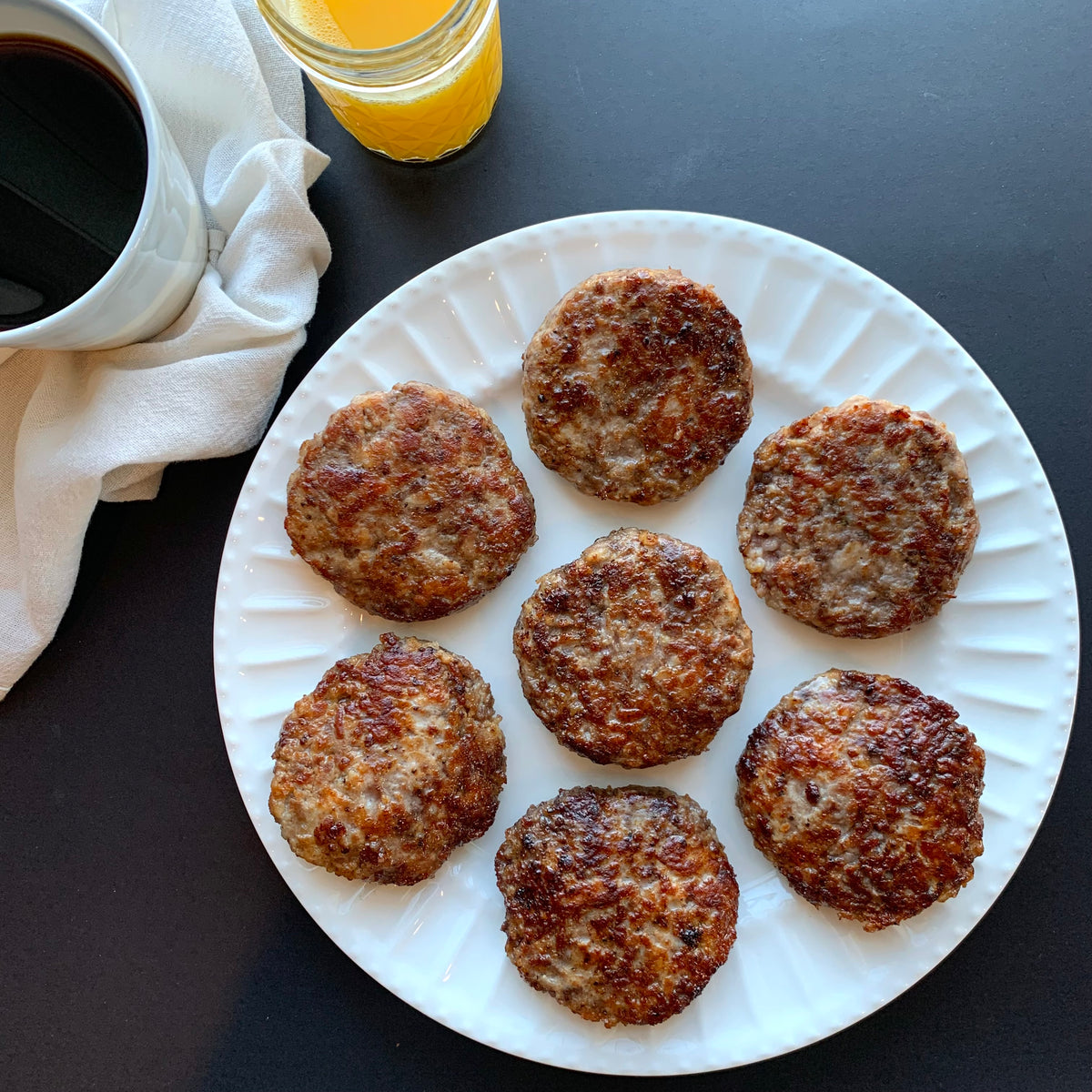 Cooked breakfast patties on a plate, styled next to a cup of coffee and orange juice